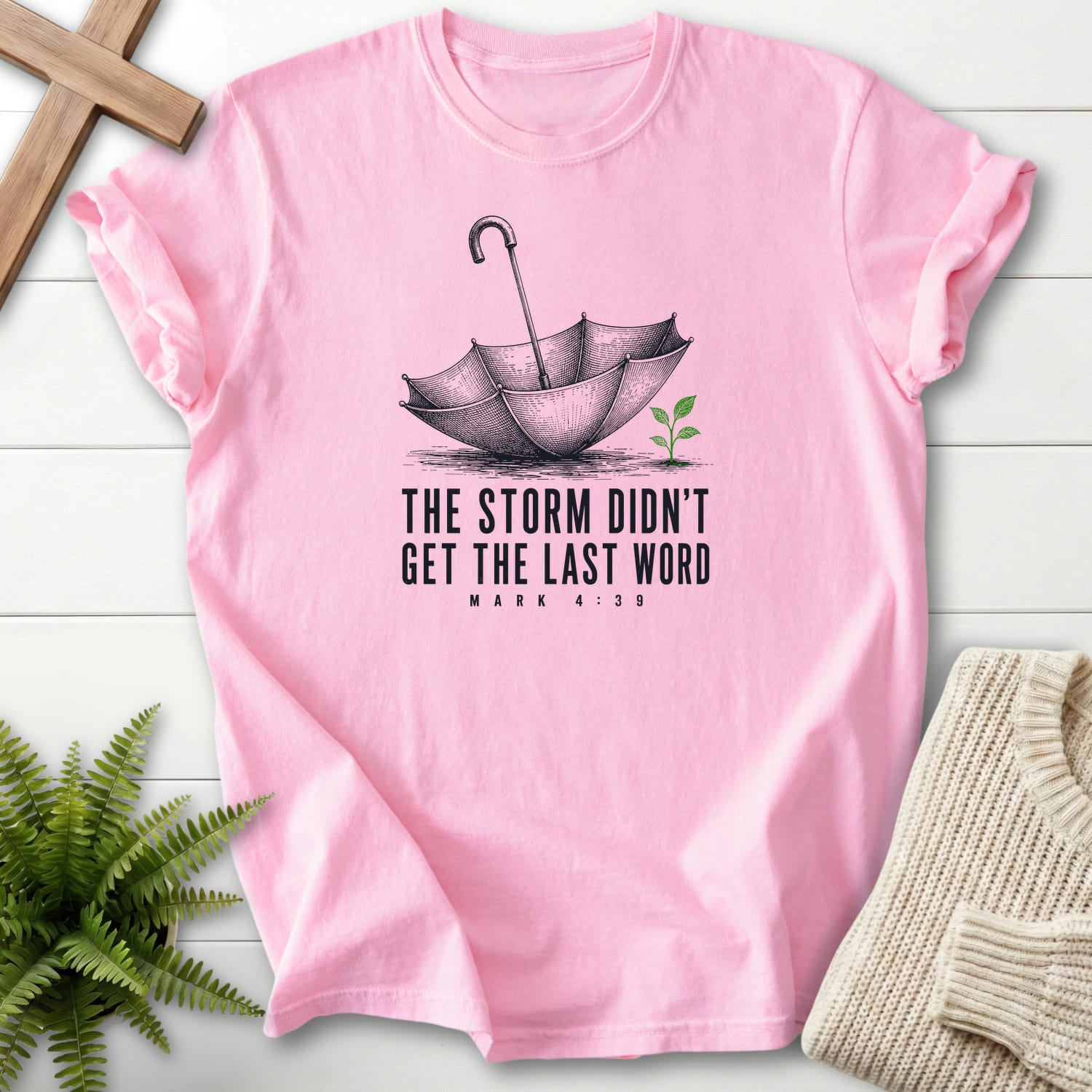Flatlay of a Blossom Comfort Colors 1717 garment-dyed Christian tee with an engraved umbrella and seedling with "Storm Didn't Get the Last Word T-Shirt".