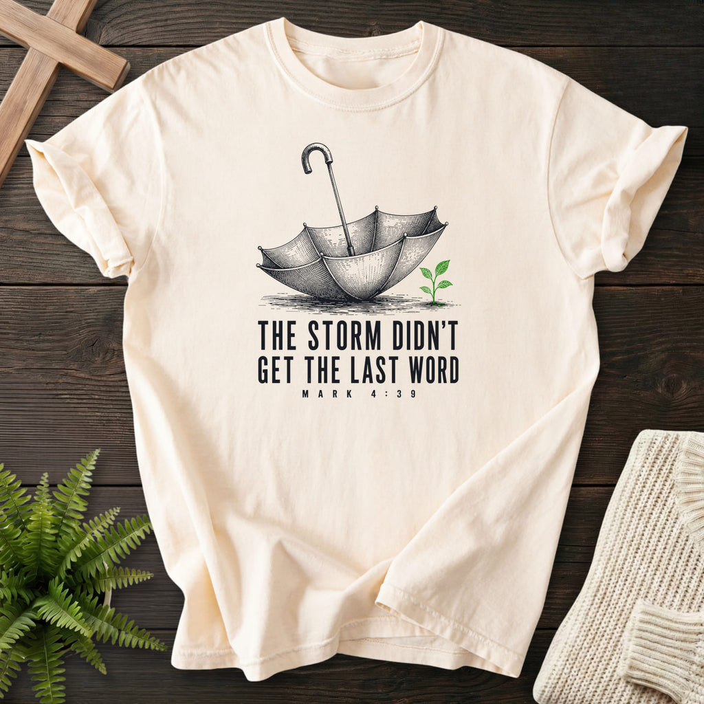 Flatlay of an Ivory faith-inspired shirt with an engraved umbrella and seedling with "Storm Didn't Get the Last Word T-Shirt".