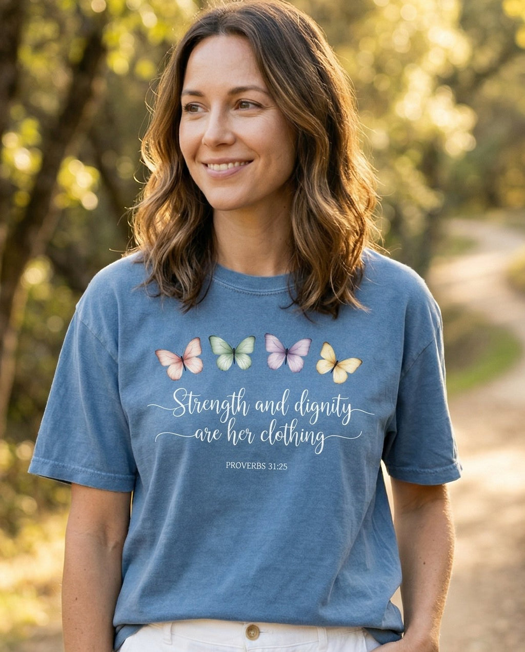 Strength and Dignity – Blue Jean women's Christian tee, lifestyle photo in nature trail – Four watercolor butterflies in pastel pink – Proverbs 31:25 – She Wears Faith