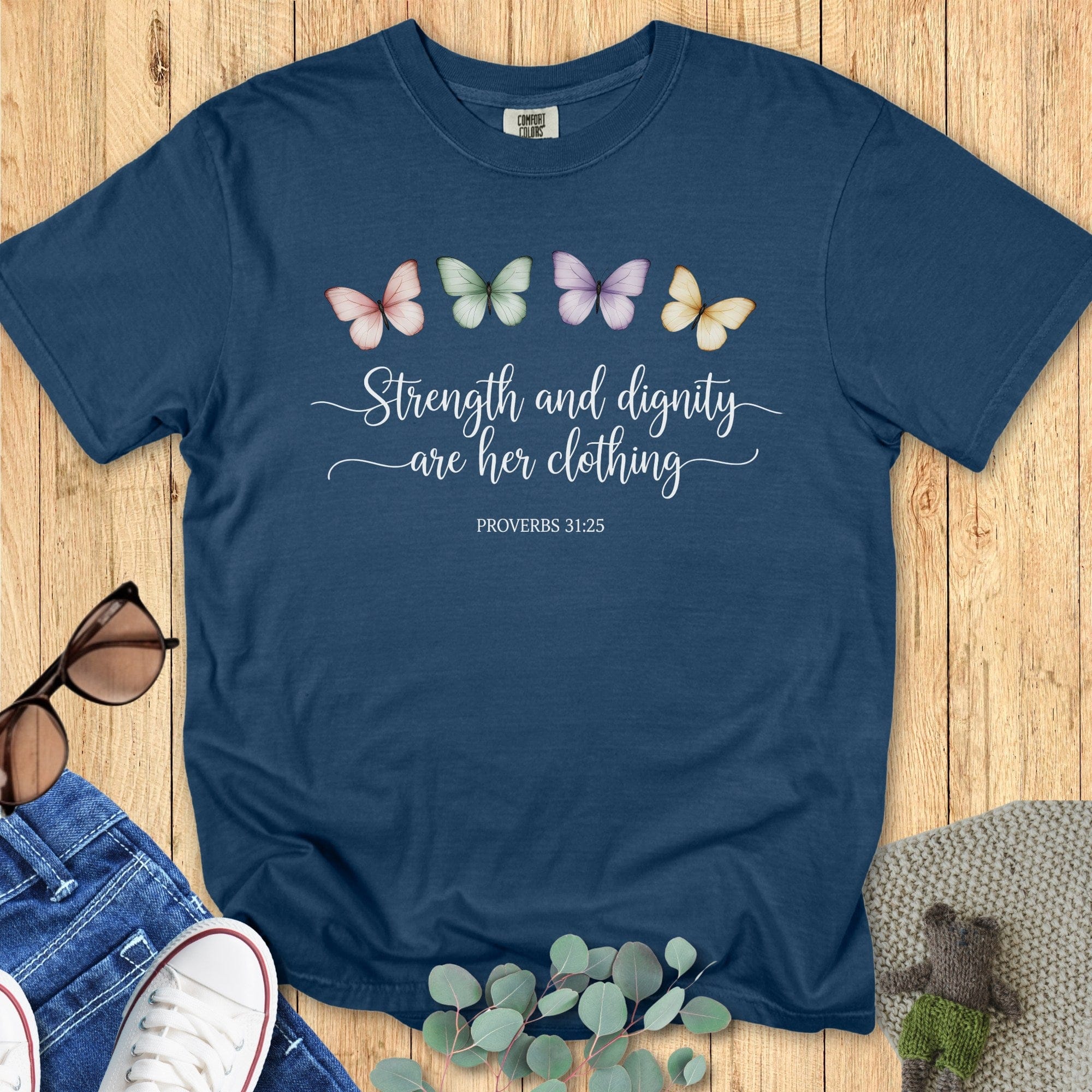 Comfort Colors 1717 midnight “Strength and dignity are her clothing – Proverbs 31:25” t-shirt with colorful butterfly design and white script lettering. A graceful women’s scripture tee — meaningful faith-based apparel for women and stylish modern Christian shirt, ideal for Christian mom gift ideas.