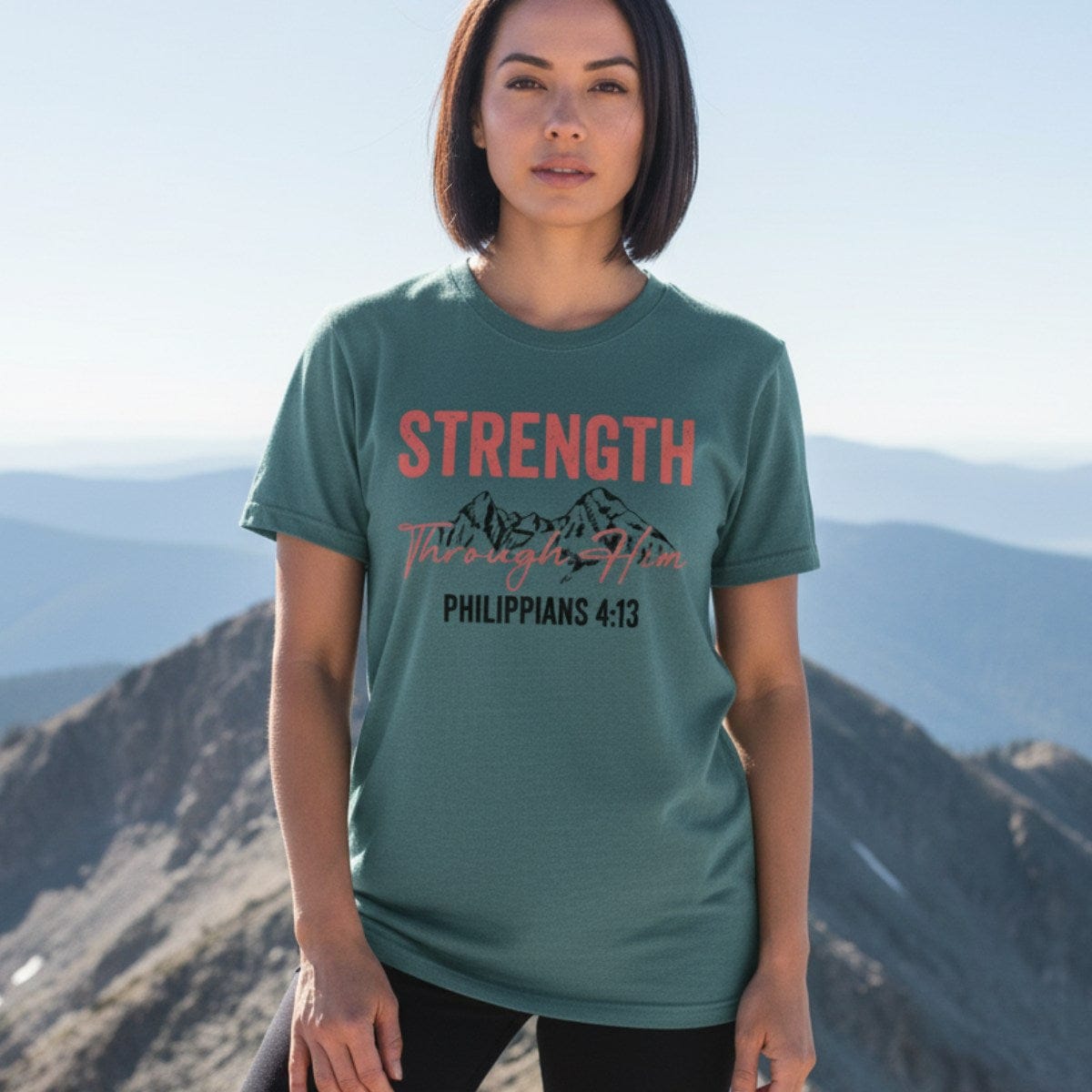 Confident woman standing on a mountain wearing a Comfort Colors 1717 blue spruce “Strength Through Him – Philippians 4:13” t-shirt. A bold and empowering women’s scripture tee — perfect modern Christian shirt and Christian mom gift idea for outdoor-loving believers.