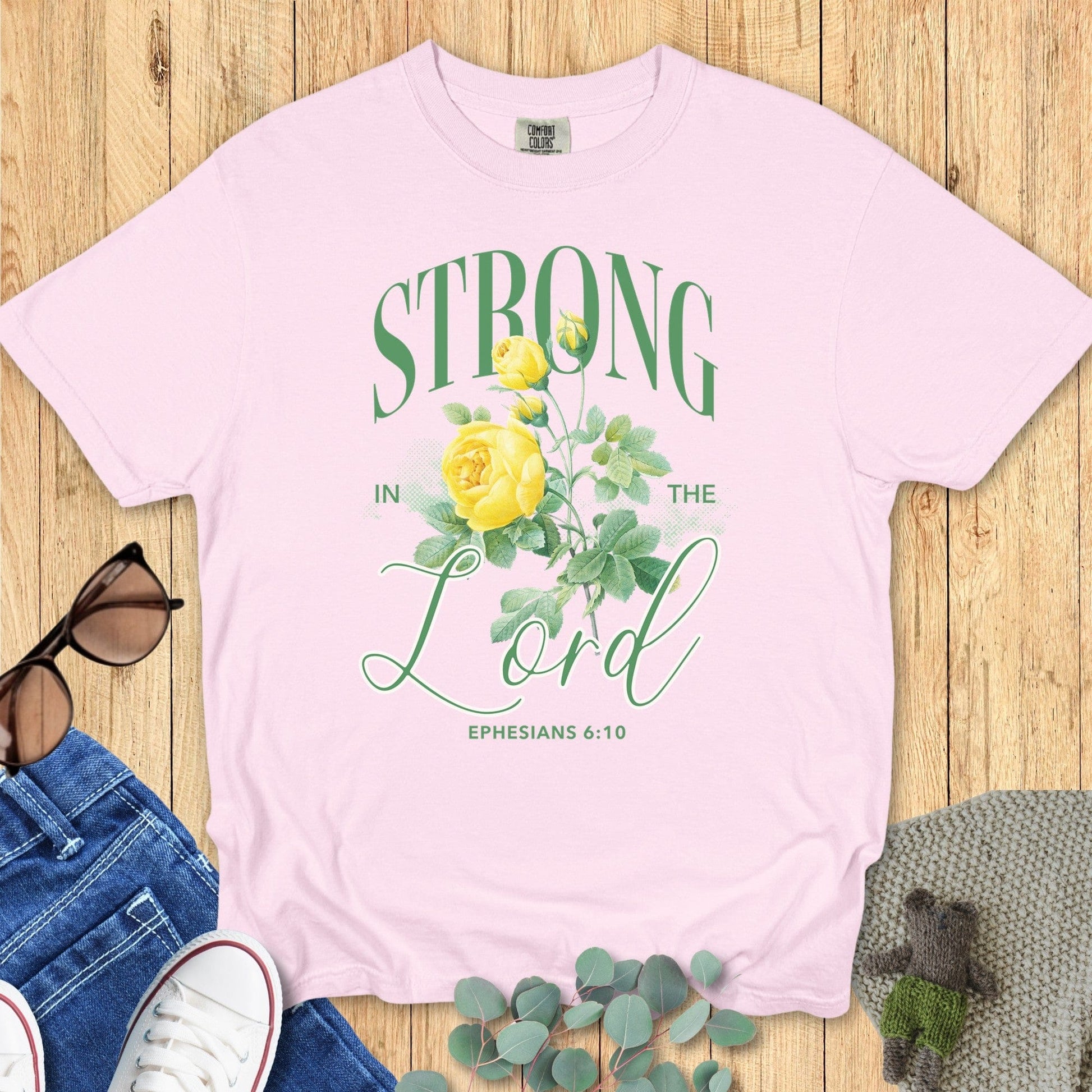 Flatlay of a Comfort Colors 1717 blossom “Strong in the Lord – Ephesians 6:10” t-shirt featuring vintage-style yellow floral design. A feminine and faith-filled women’s scripture tee — uplifting faith-based apparel for women and perfect Christian mom gift.