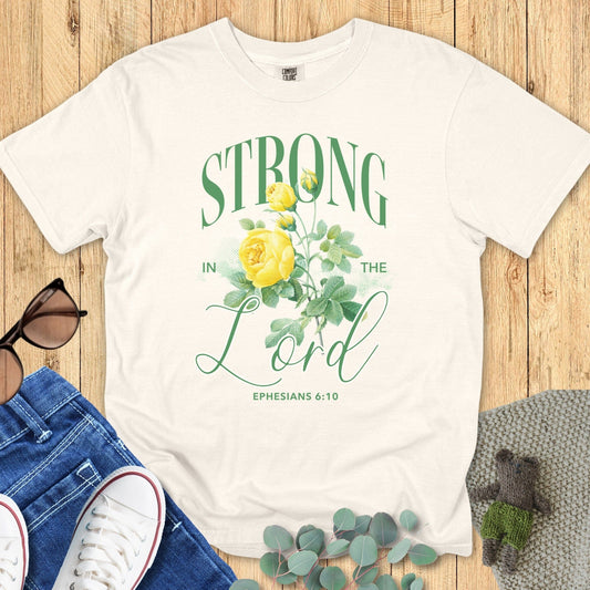 Flatlay of a Comfort Colors 1717 ivory “Strong in the Lord – Ephesians 6:10” t-shirt featuring elegant green lettering and yellow rose illustration. A soft and uplifting women’s scripture tee — faith-based apparel for women and a meaningful Christian mom gift idea.