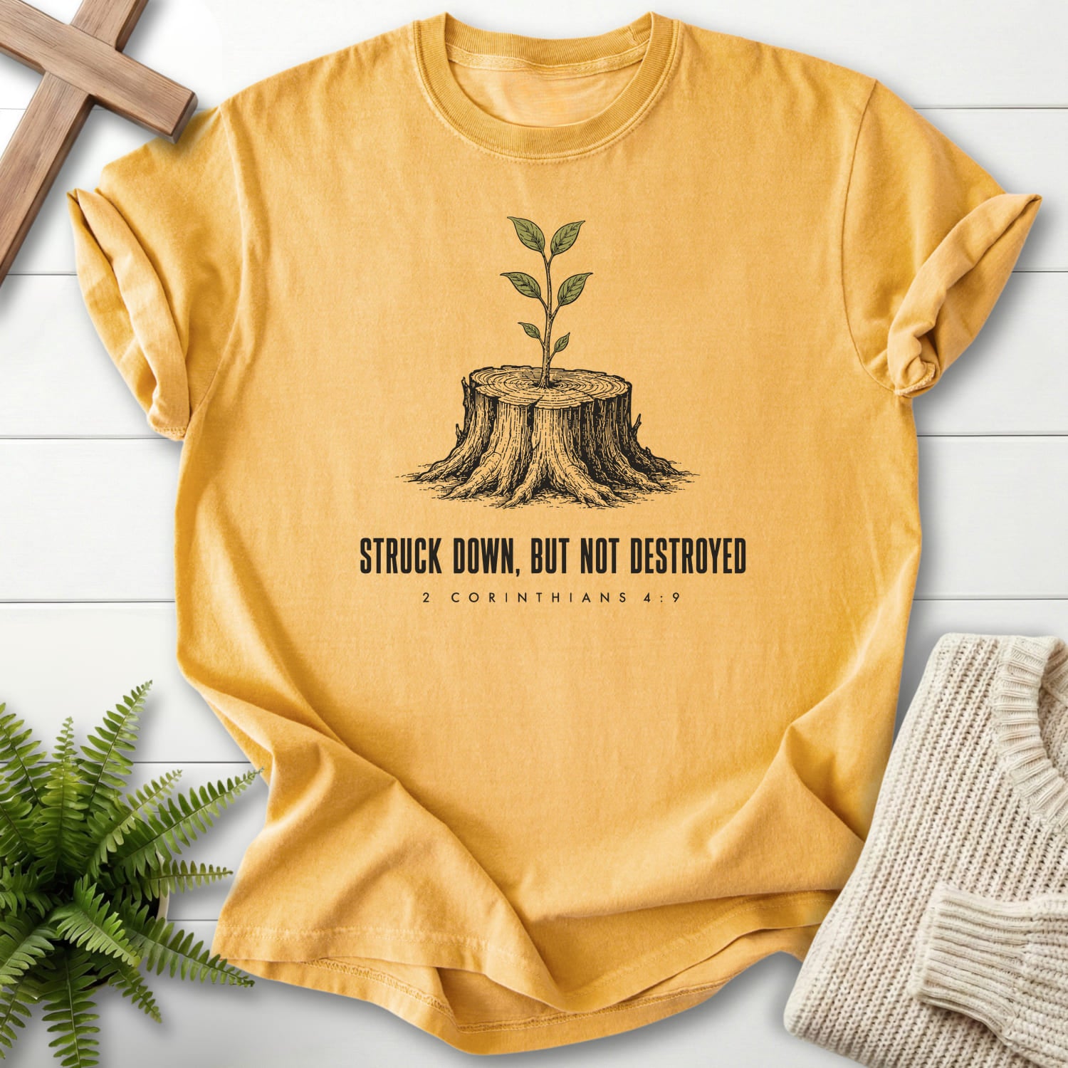 Flatlay of a Mustard women's Christian tee with "Struck Down But Not Destroyed T-Shirt" design.