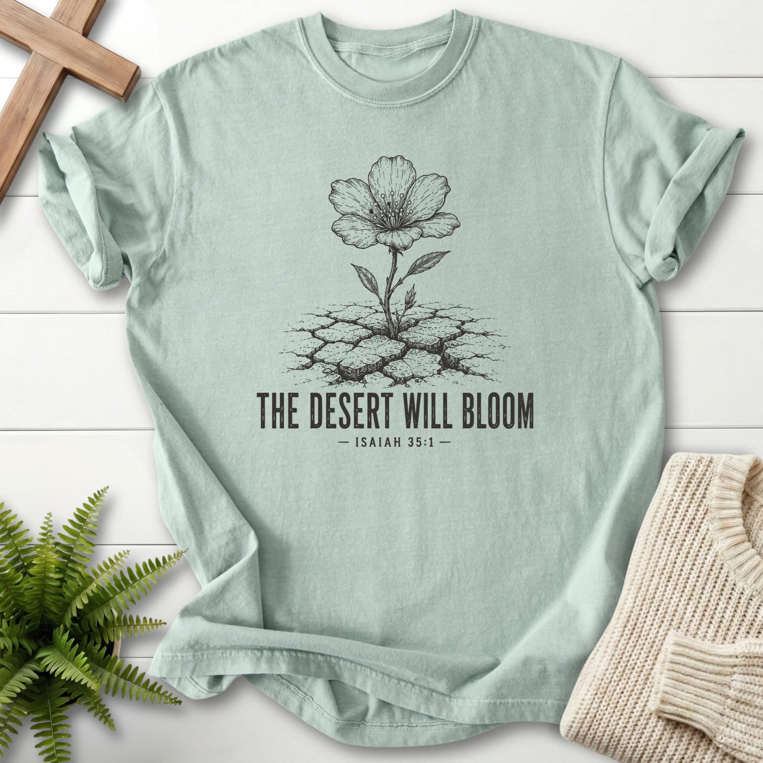 Flat lay of a Bay faith-inspired shirt featuring flower artwork with "The Desert Will Bloom T-Shirt".