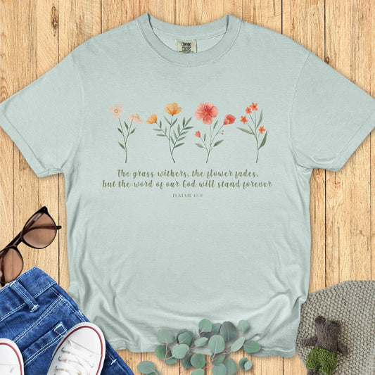 Flatlay of a Comfort Colors 1717 bay blue “The Grass Withers, The Flower Fades – Isaiah 40:8” t-shirt with hand-drawn floral details. A modern Christian shirt that blends timeless faith with a fresh botanical look.