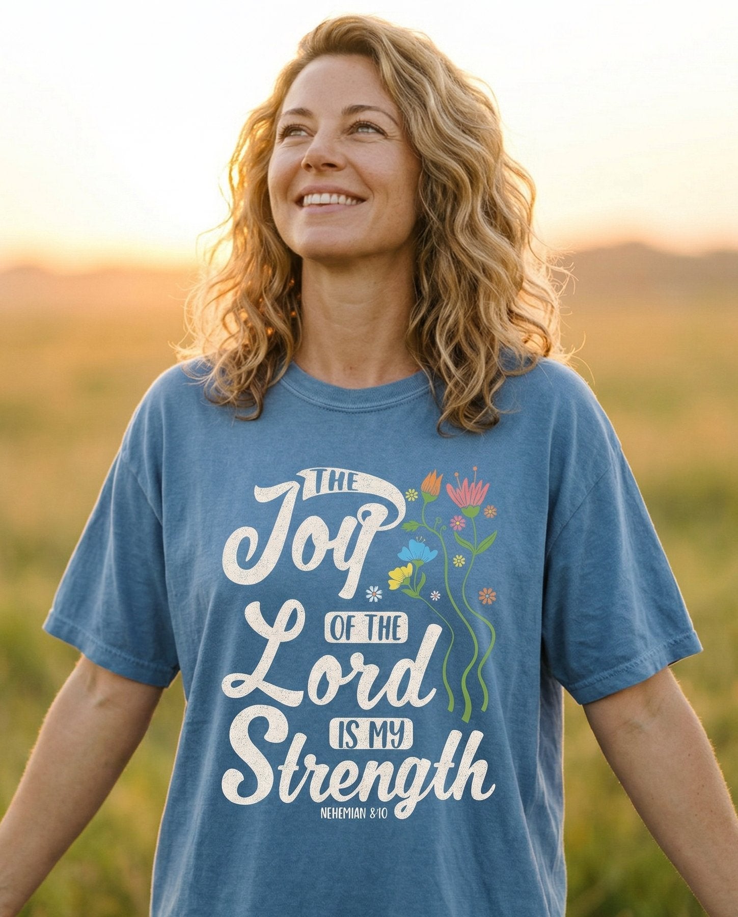 Joy of the Lord – Blue Jean women's Christian tee, lifestyle photo in wildflower meadow at sunrise – Flowing script lettering 'The Joy of the Lord Is My Strength' with col – Nehemiah 8:10 – She Wears Faith
