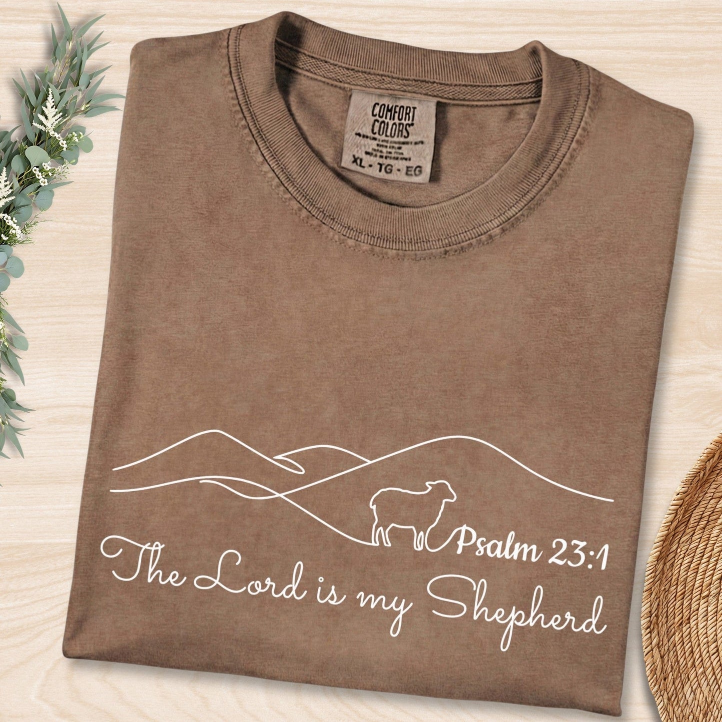 Flat lay of an Espresso Brown Comfort Colors 1717 tshirt with white minimalist typography and a sheep graphic. A cozy Christian women tee featuring "The Lord is my Shepherd," ideal for US faith wear apparel.