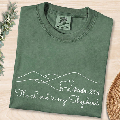 Flat lay of a Moss Green Comfort Colors 1717 tshirt displaying a simple sheep outline and Bible verse. A nature-inspired Christian women tee with Psalm 23:1, designed for US faith wear collections.