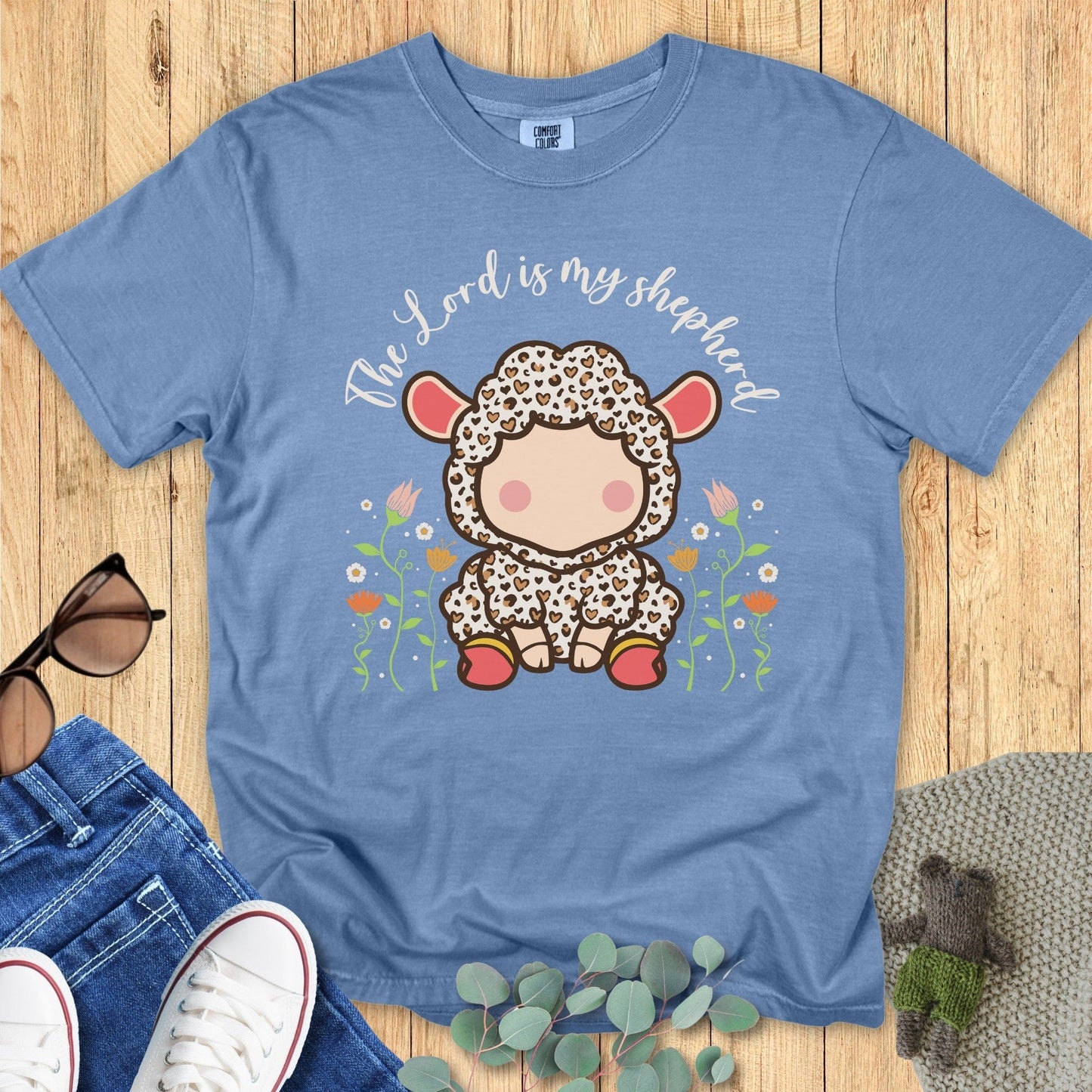 Flatlay of a Comfort Colors 1717 blue jean “The Lord Is My Shepherd” t-shirt featuring a soft pastel lamb illustration. A charming women’s scripture tee that blends comfort, faith, and modern Christian style — ideal for Christian mom gift ideas.