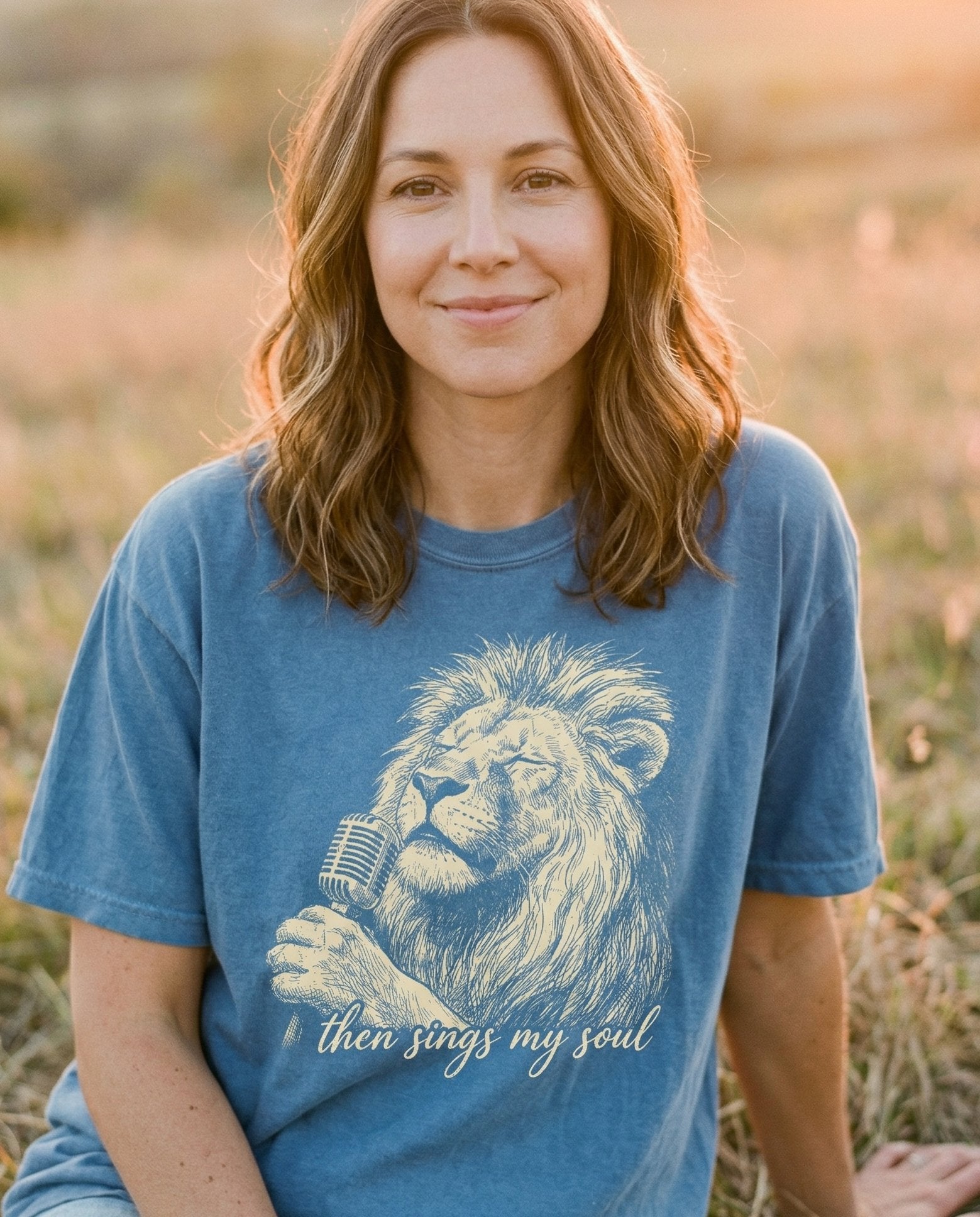 Then Sings My Soul – Blue Jean women's Christian tee, lifestyle photo in wildflower meadow at sunrise – Vintage line-art illustration of a majestic lion holding a vintage mic – She Wears Faith