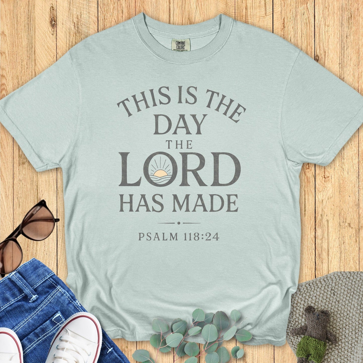 Comfort Colors 1717 bay blue “This Is The Day The Lord Has Made – Psalm 118:24” t-shirt with minimalist sunrise artwork. A modern Christian shirt that inspires daily thankfulness and faith.
