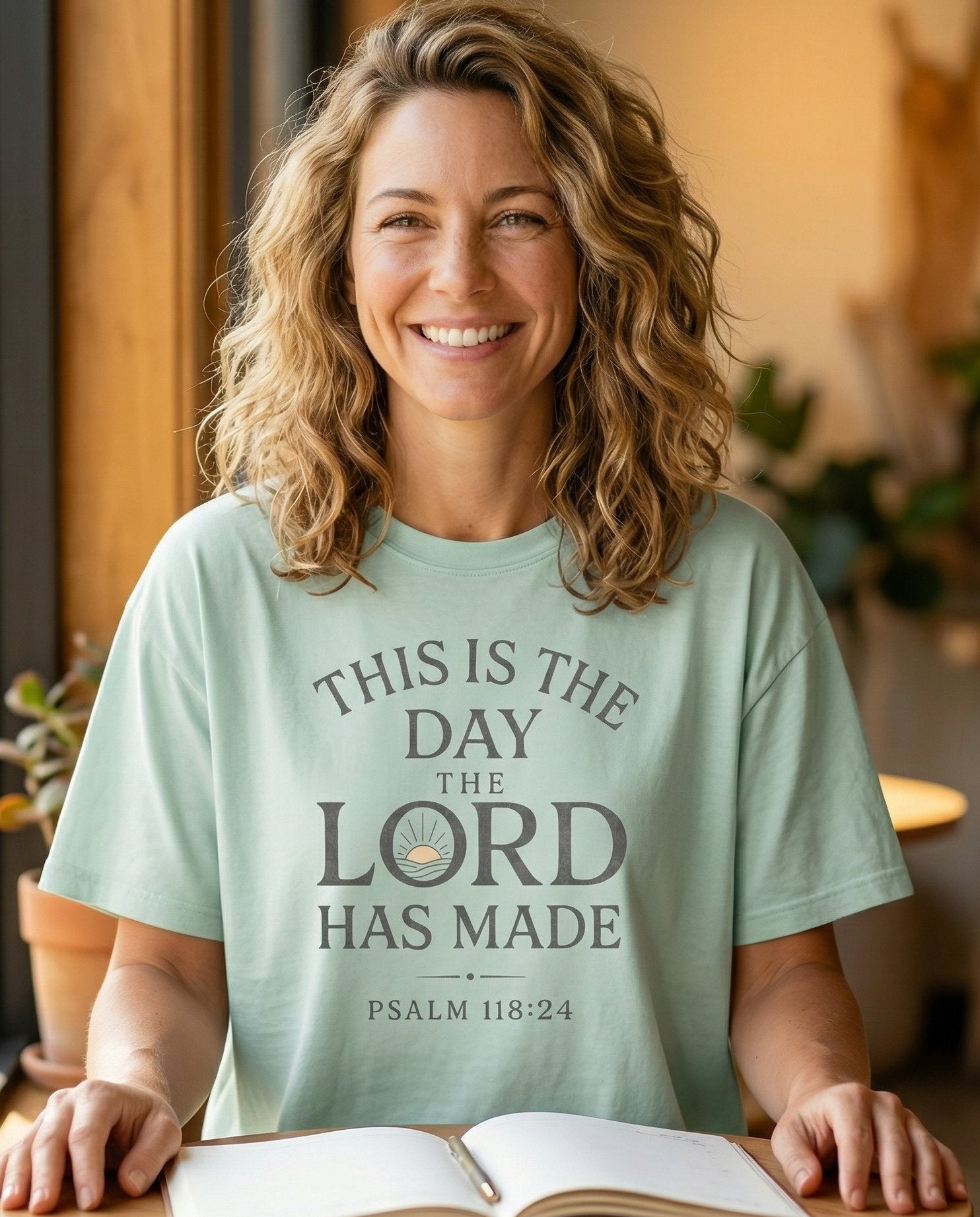 This is the Day – Bay women's Christian tee, lifestyle photo in cozy café – Bold stacked typography 'This Is the Day the Lord Has Made' with a sma – Psalm 118:24 – She Wears Faith
