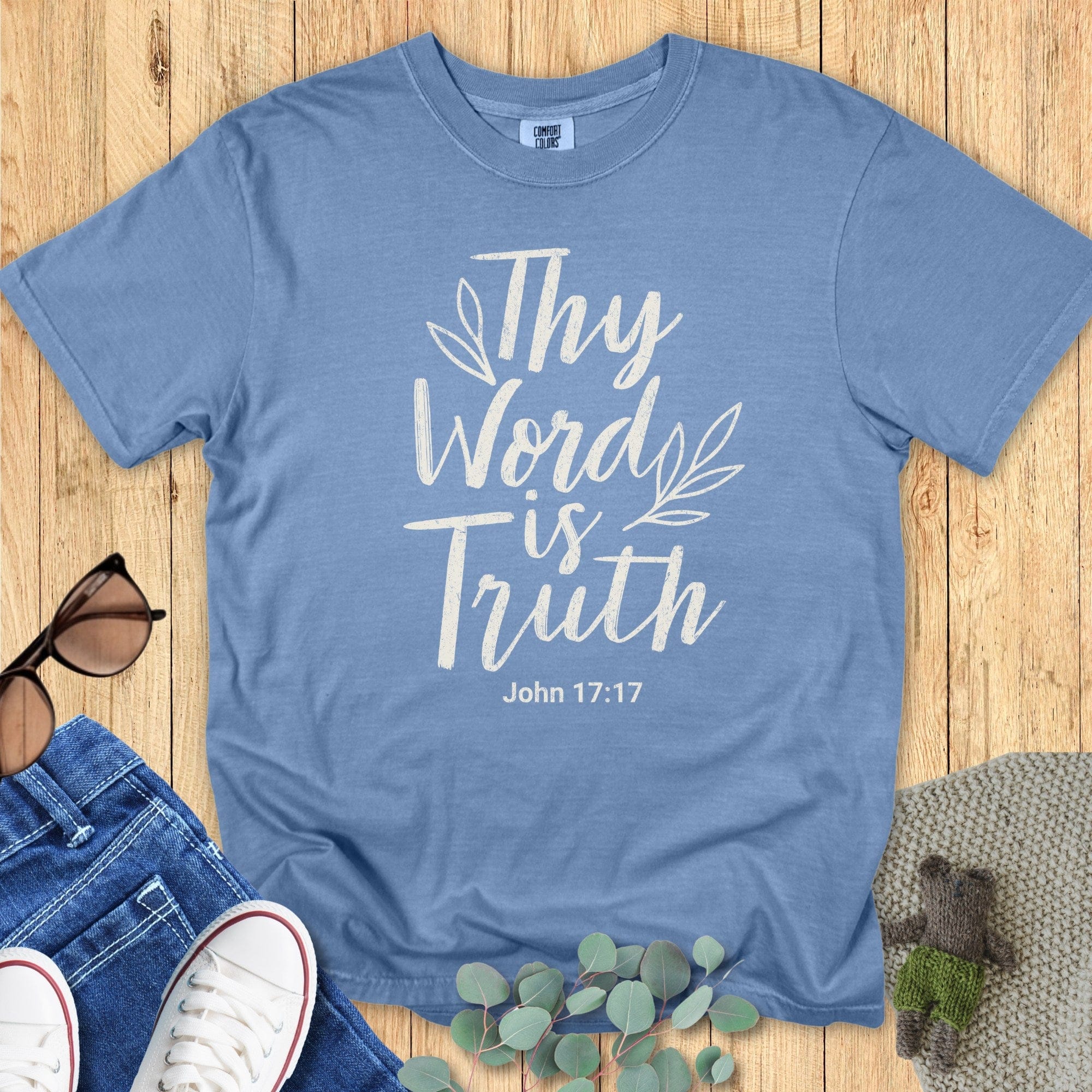 Flatlay of a Comfort Colors 1717 blue jean “Thy Word Is Truth – John 17:17” t-shirt featuring cream lettering and simple leaf design. A beautiful women’s scripture tee — uplifting faith-based apparel for women and stylish modern Christian shirt, great Christian mom gift idea.
