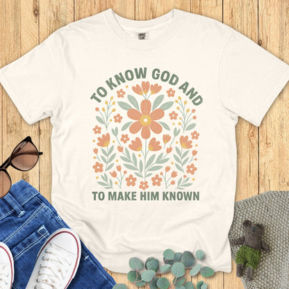 Flatlay of a Comfort Colors 1717 ivory “To Know God and To Make Him Known” t-shirt with soft pastel floral design. A beautiful women’s scripture tee — faith-based apparel for women and modern Christian shirt, ideal Christian mom gift idea.