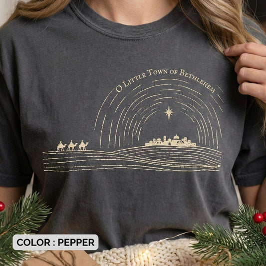 Close-up of a Comfort Colors 1717 pepper Christian women’s T-shirt with a minimalist gold Bethlehem nativity scene and star illustration. Features the phrase “O Little Town of Bethlehem.” A soft US faith wear Christmas tee with vintage texture and sacred holiday symbolism.