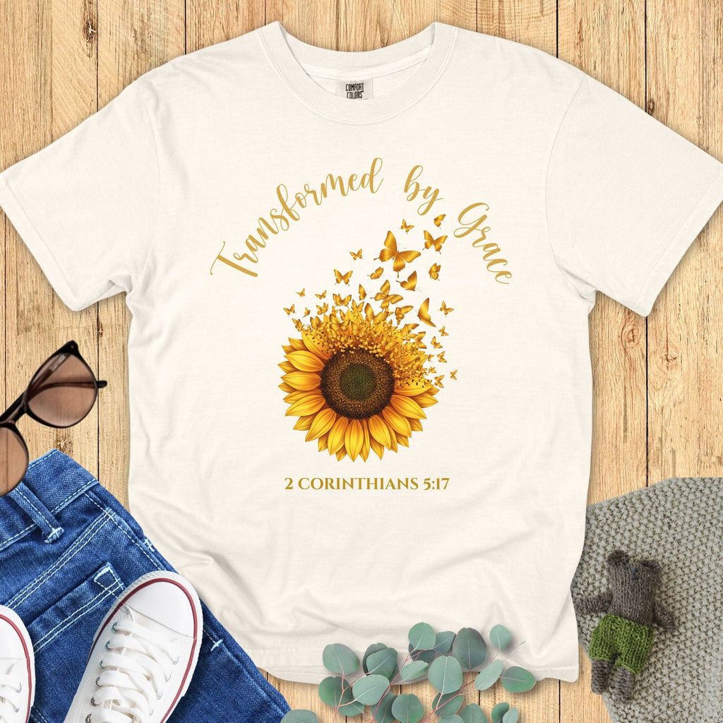 Comfort Colors 1717 Christian women t-shirt in ivory flat lay. Christian sunflower graphic with butterflies and scripture text “Transformed by Grace – 2 Corinthians 5:17