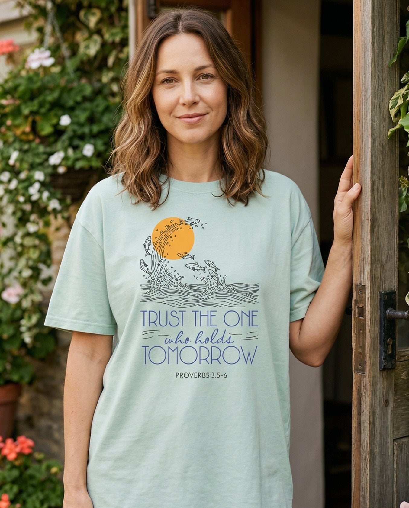Trust the One who holds Tomorrow – Bay women's Christian tee, lifestyle photo in cottage doorway – Line-art illustration of fish leaping from ocean waves around a golden – Proverbs 3:5-6 – She Wears Faith
