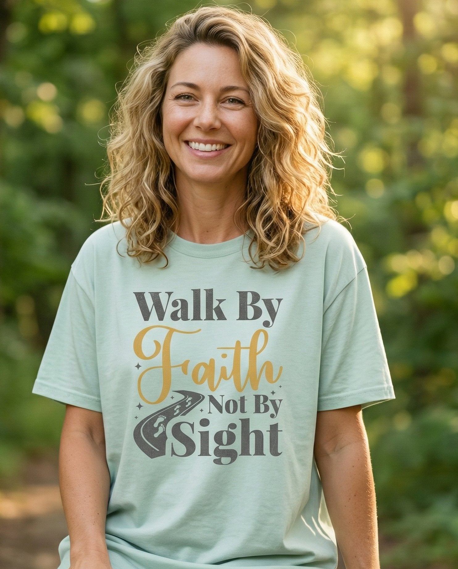 Walk By Faith – Bay women's Christian tee, lifestyle photo in nature trail – Mixed-font design reading 'Walk By Faith Not By Sight' in gray and gol – 2 Corinthians 5:7 – She Wears Faith