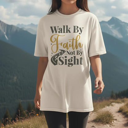 Christian woman wearing a Comfort Colors Christian t-shirt with the phrase 'Walk By Faith Not By Sight' in gold and gray lettering, styled with a road and footprints graphic, photographed outdoors on a mountain trail