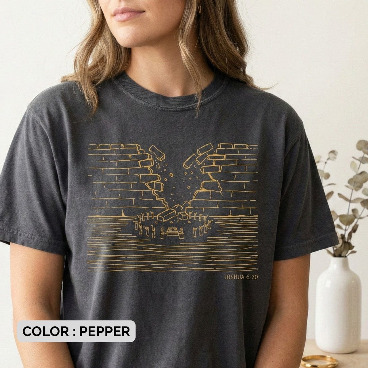 Woman wearing a Pepper Grey Comfort Colors 1717 tshirt featuring a gold line drawing of the walls of Jericho crumbling. A powerful Christian women tee with Joshua 6:20 scripture, designed for bold US faith wear collections.