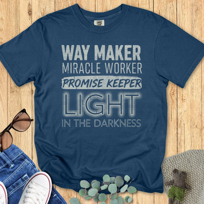 Comfort Colors Christian t-shirt in midnight blue with bold typography design featuring the worship phrase 'Way Maker, Miracle Worker, Promise Keeper, Light in the Darkness.' Faith-based apparel styled flat lay with casual jeans and sneakers.