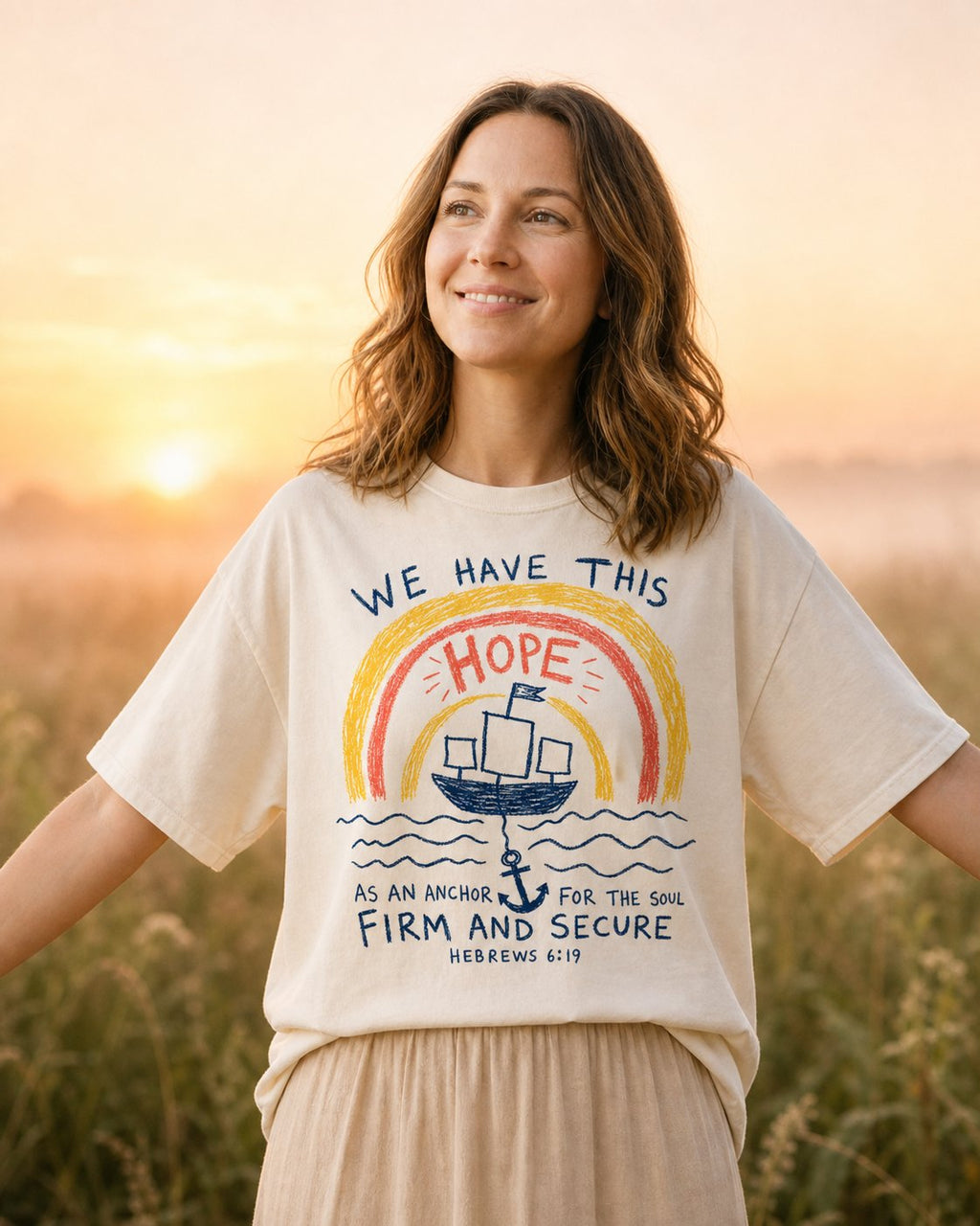 We Have This Hope – Ivory women's Christian tee, lifestyle photo in wildflower meadow at sunrise – Childlike crayon rainbow sailboat and anchor drawing – Hebrews 6:19 – She Wears Faith