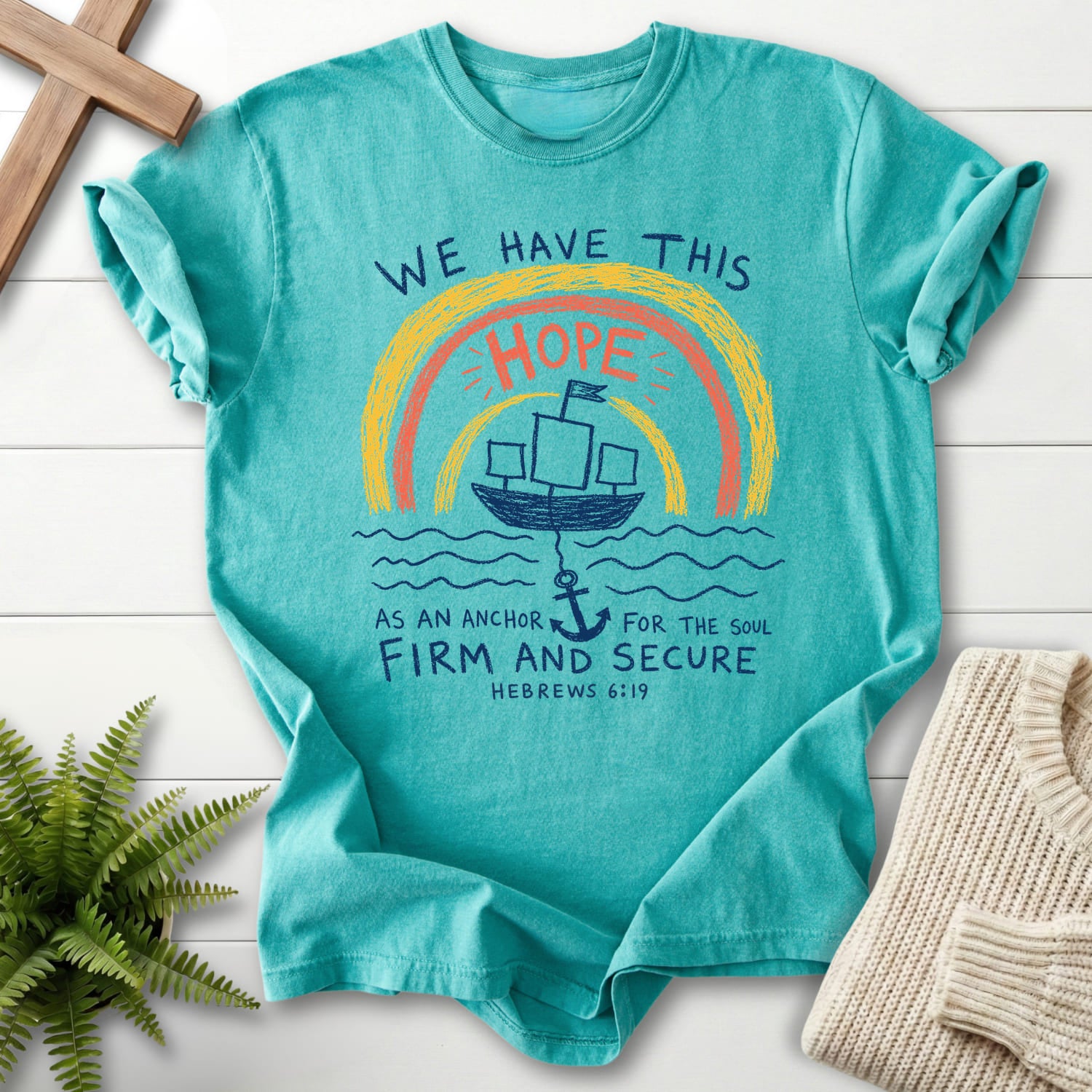 Flatlay of a Seafoam Comfort Colors 1717 Bible verse tee with "WE HAYE THIS T-Shirt" Hebrews 6:19.