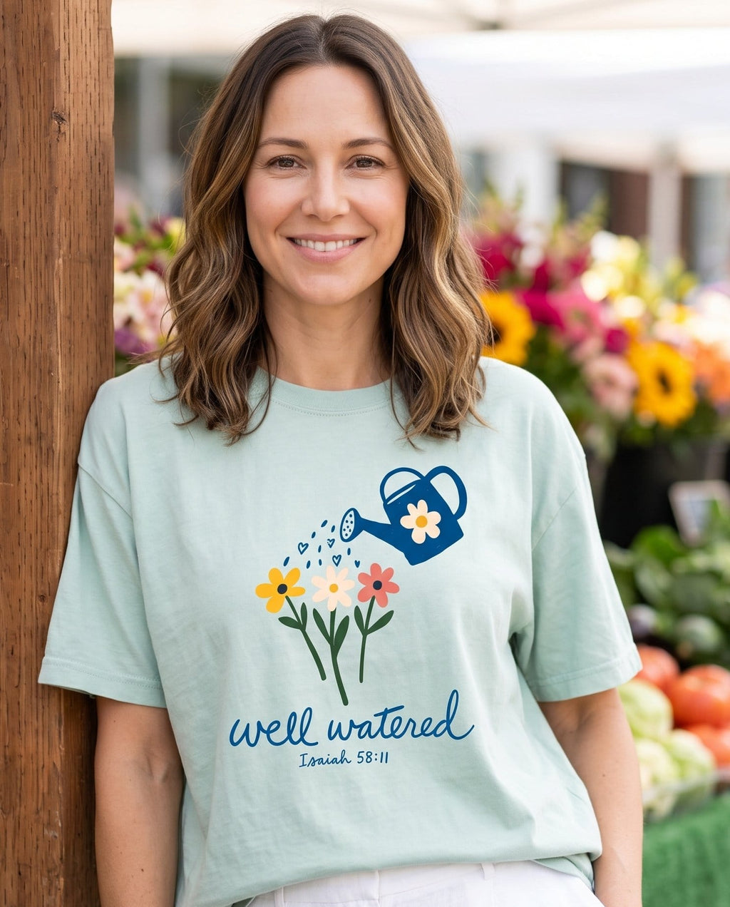 Well Watered Isaiah 58:11 – Bay women's Christian tee, lifestyle photo in farmers market – Hand-drawn blue watering can showering heart-shaped drops over three b – Isaiah 58:11 – She Wears Faith
