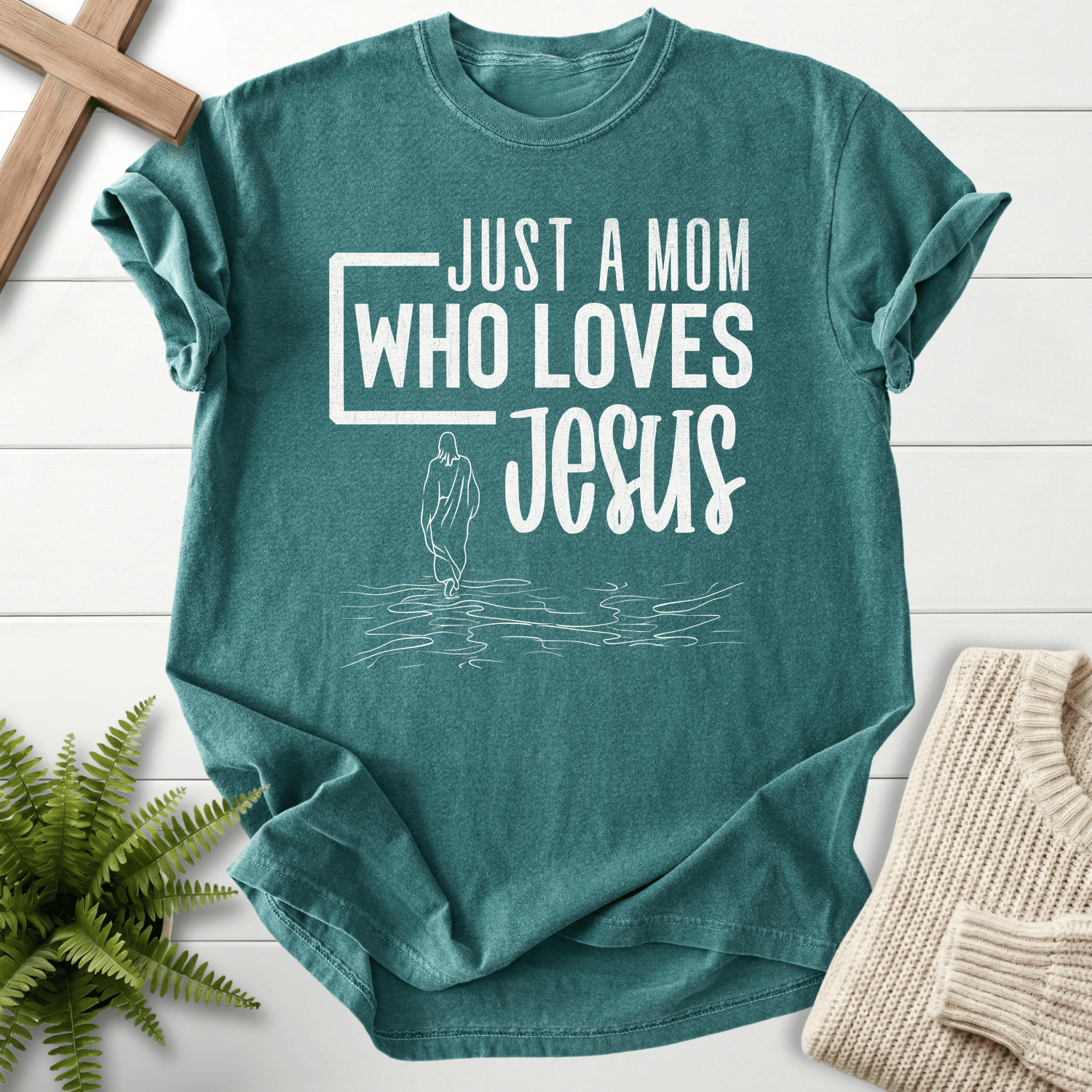 Blue Spruce women's Christian t-shirt with 'Just a Mom Who Loves Jesus' block lettering and water silhouette.