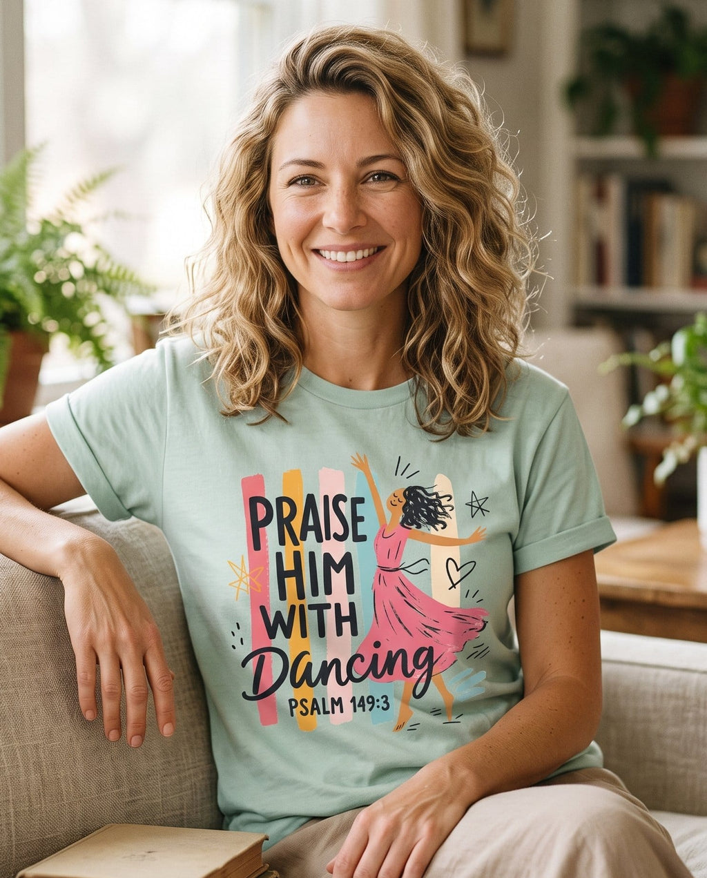 Worship Dance – Bay women's Christian tee, lifestyle photo in cozy living room – Illustrated woman twirling in a flowing pink dress against a colorful  – Psalm 149:3 – She Wears Faith