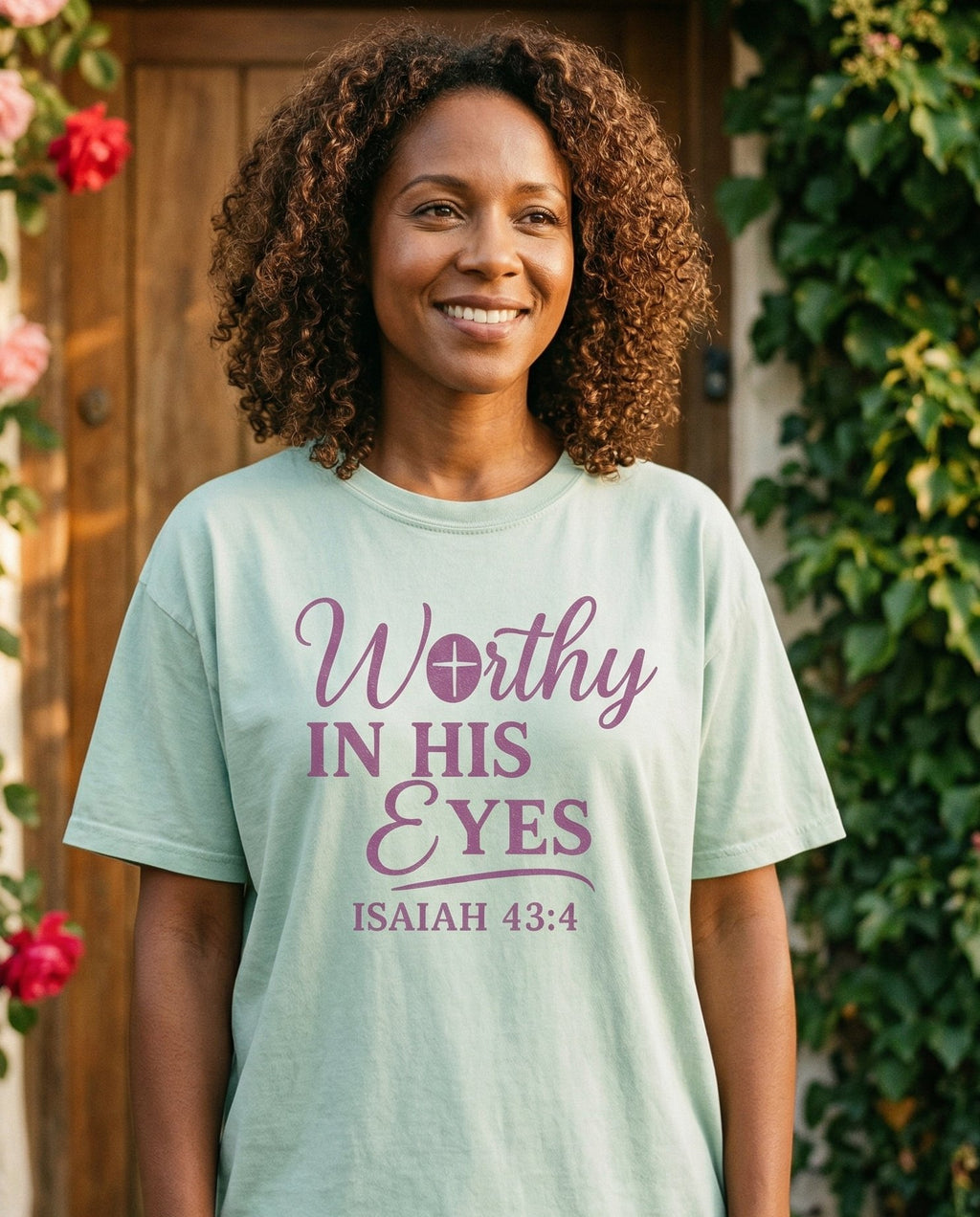 Worthy in His Eyes – Bay women's Christian tee, lifestyle photo in cottage doorway – Purple serif script 'Worthy in His Eyes' with a cross detail in the W – Isaiah 43:4 – She Wears Faith