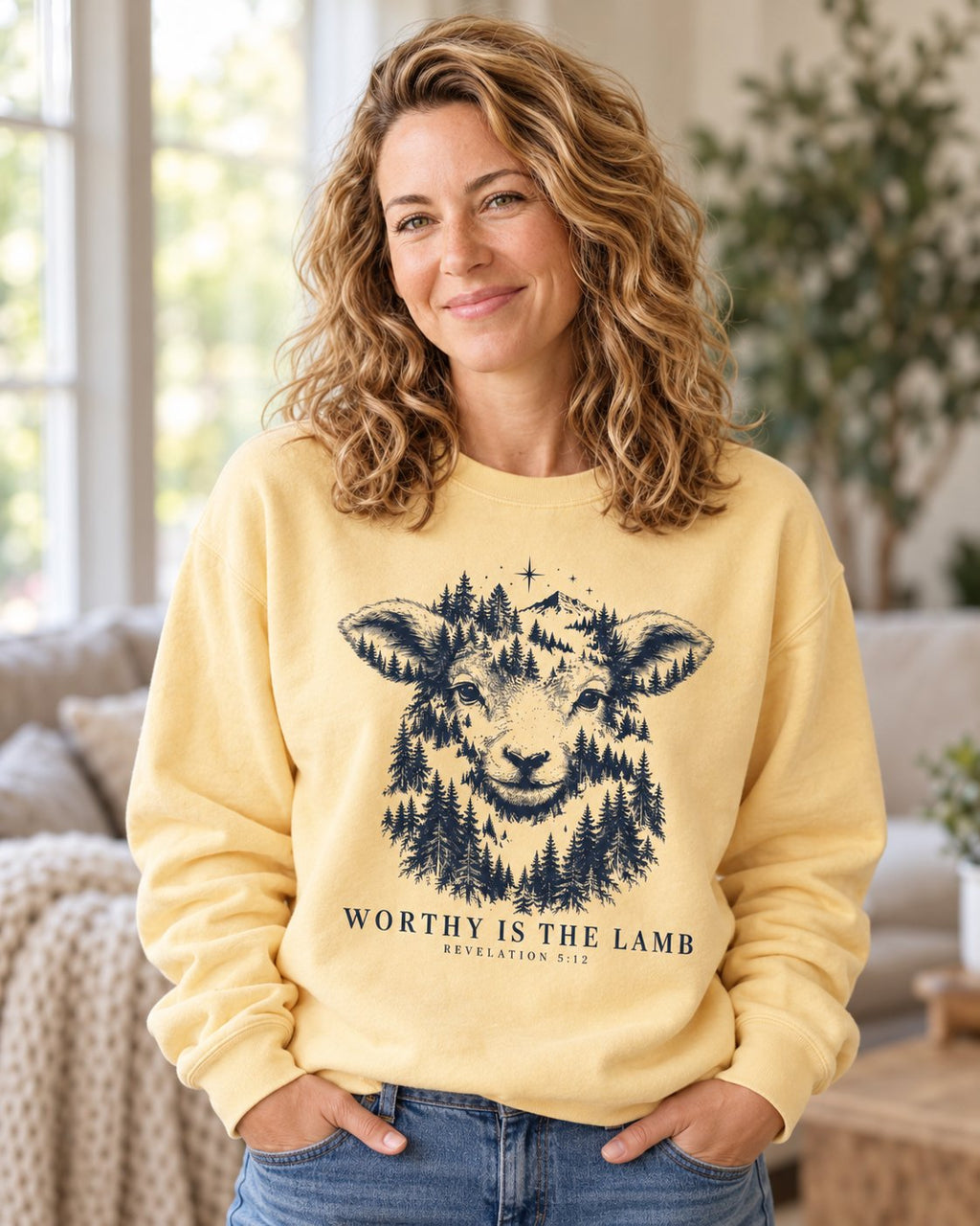 Worthy Is the Lamb, Butter women's Christian sweatshirt, lifestyle photo in cozy living room, lamb face filled with a pine forest and WORTHY IS THE LAMB, Revelation 5:12, She Wears Faith