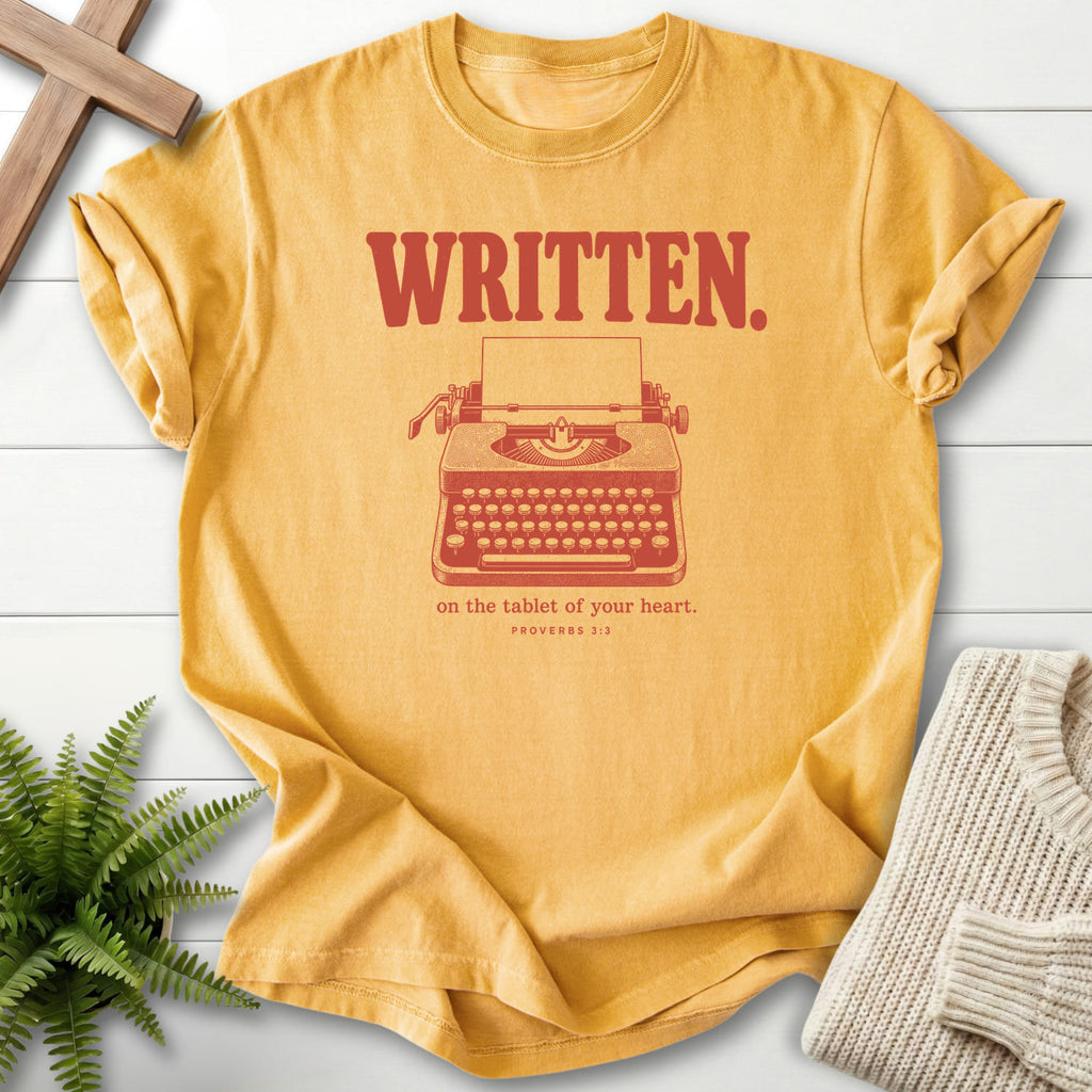 Flatlay of a Mustard Christian graphic tee with "Written on the Tablet of Your T-Shirt" Proverbs 3:3.