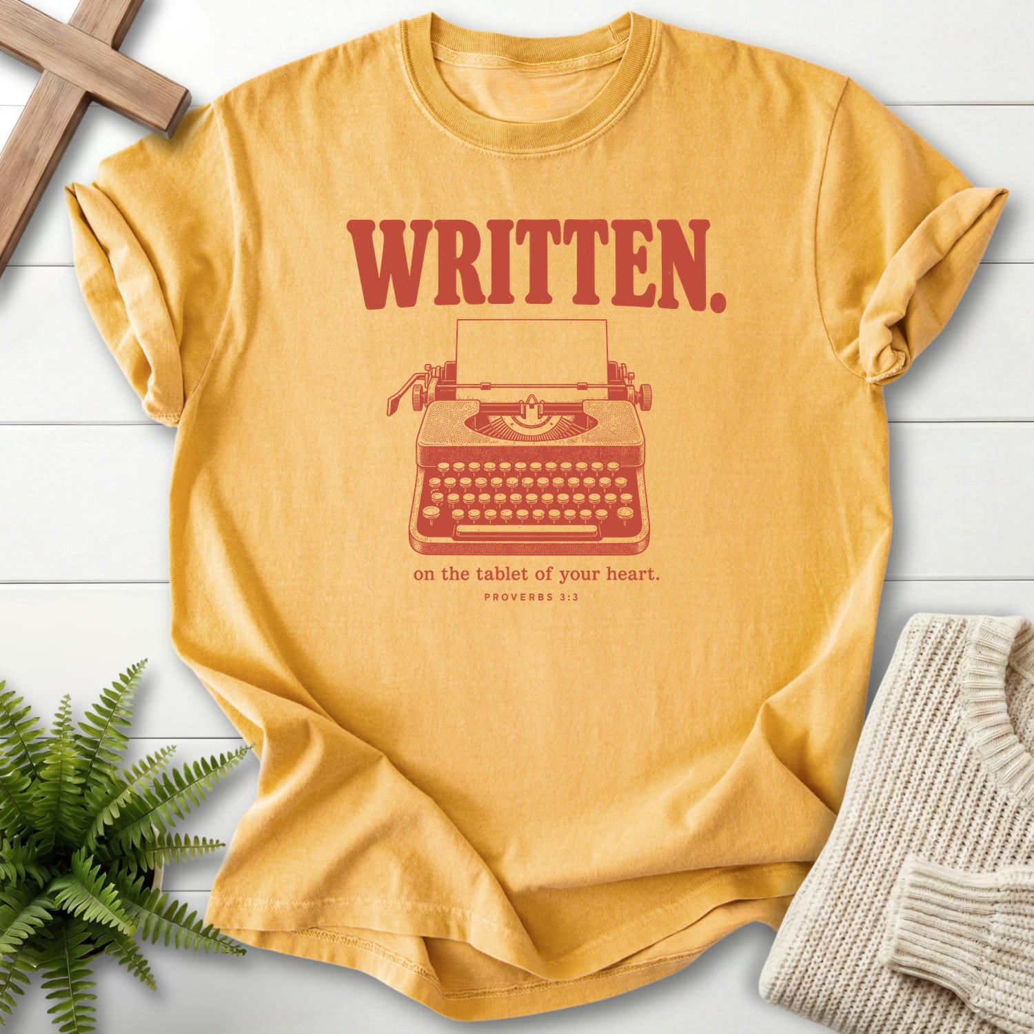 Flatlay of a Mustard Christian graphic tee with "Written on the Tablet of Your T-Shirt" Proverbs 3:3.