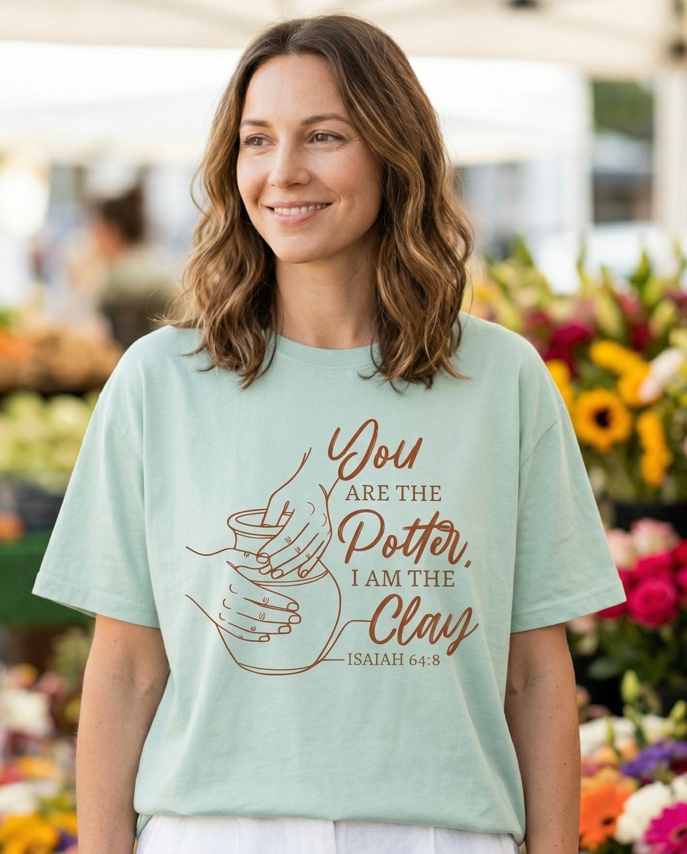 You Are The Potter – Bay women's Christian tee, lifestyle photo in farmers market – Warm terracotta-tone line art of hands shaping a clay pot on a wheel w – Isaiah 64:8 – She Wears Faith
