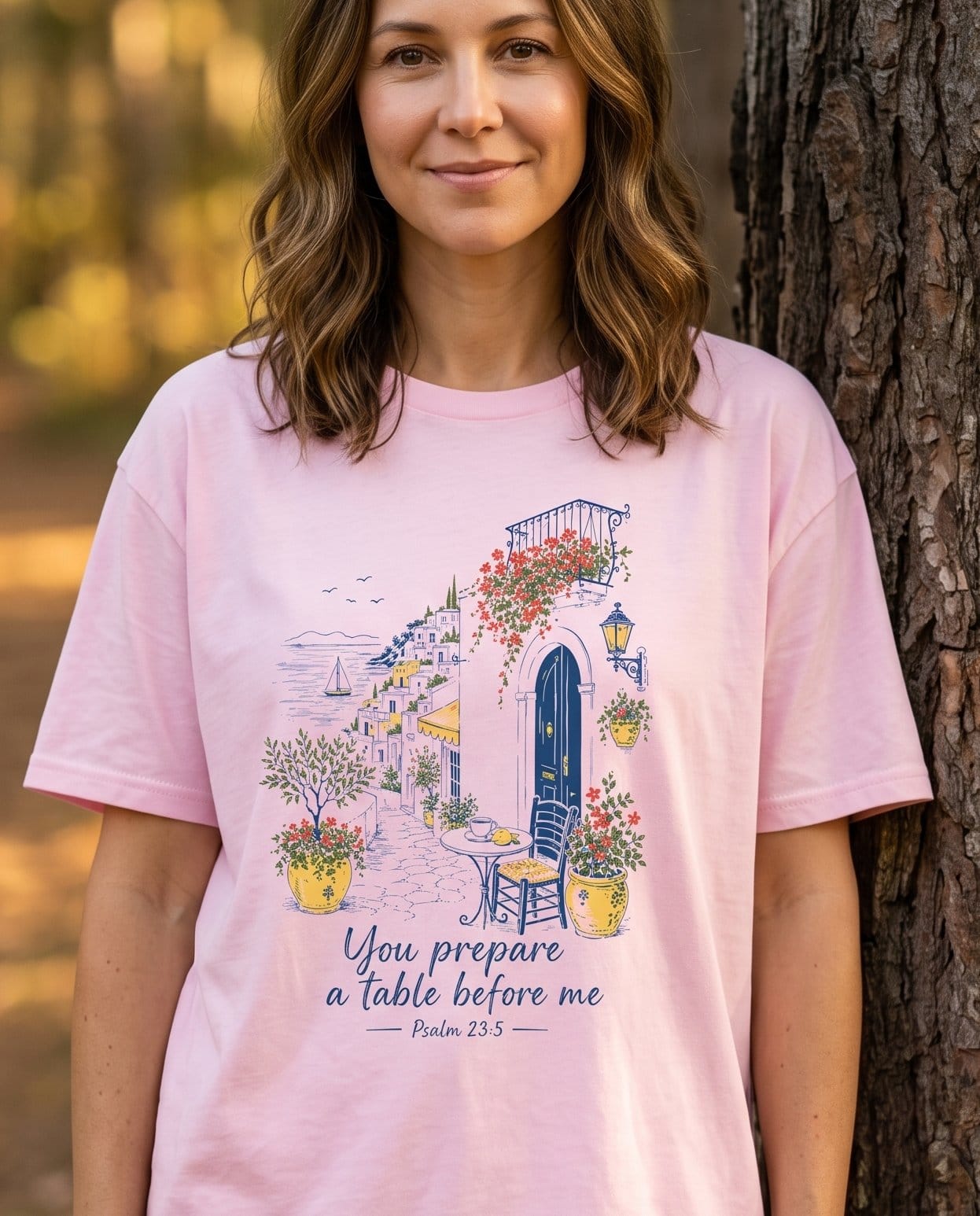 You Prepare a Table Before Me Psalm 23:5 – Blossom women's Christian tee, lifestyle photo in nature trail – Sunlit Mediterranean village illustration in blue ink and warm yellow  – Psalm 23:5 – She Wears Faith